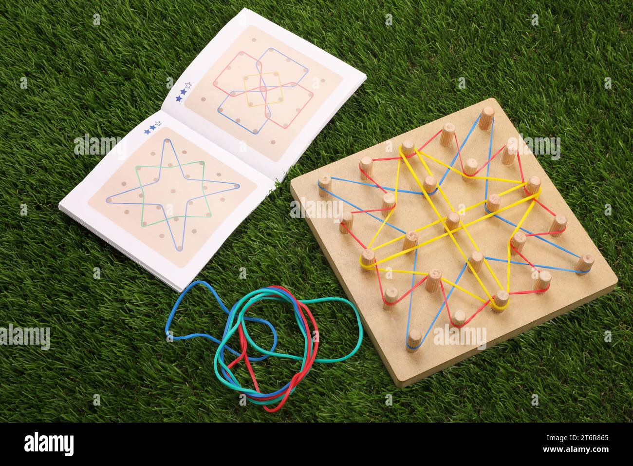 Wooden geoboard with rubber bands and activity book on artificial grass. Educational toy for motor skills development Stock Photo