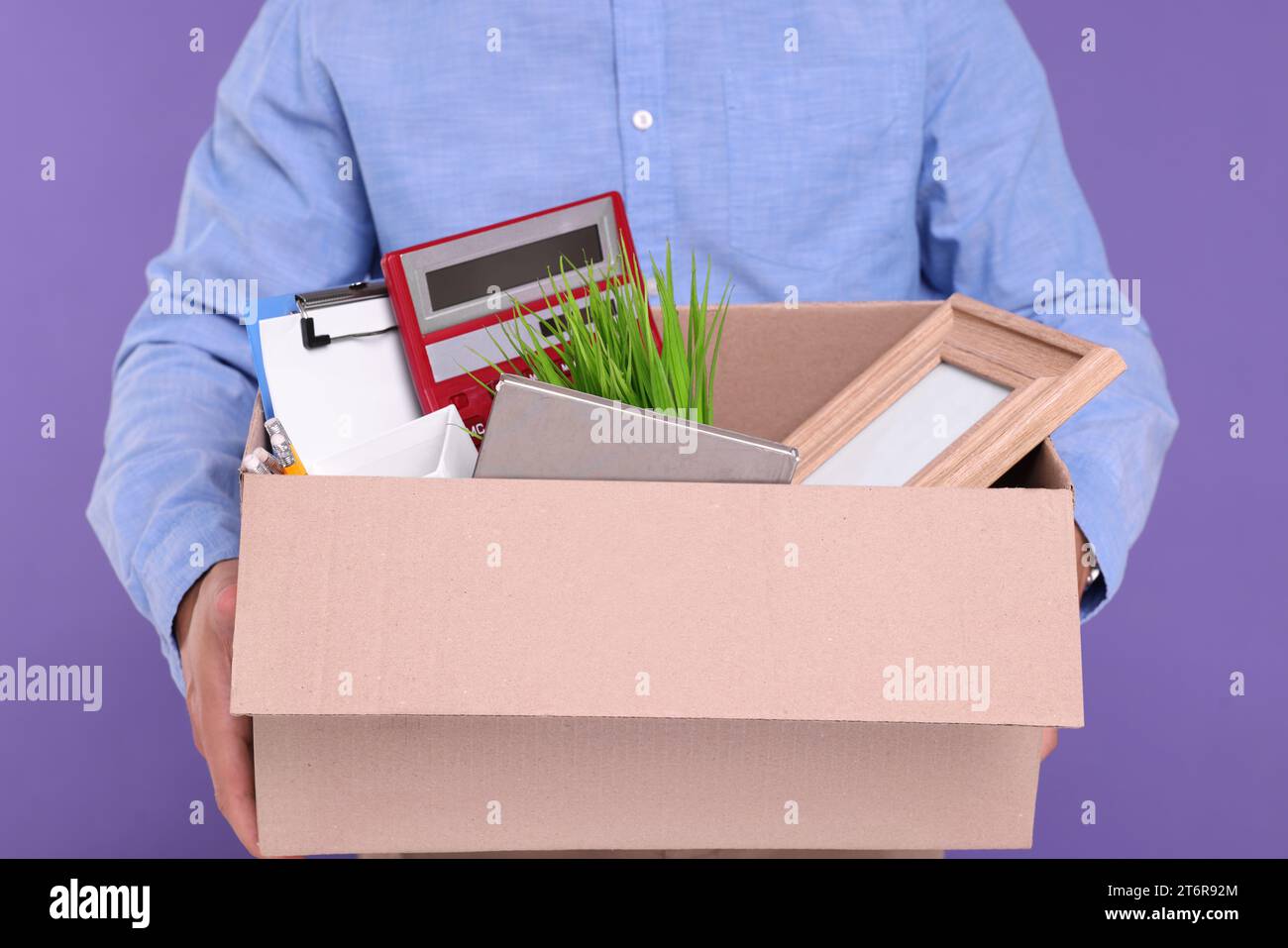 Unemployed man with box of personal office belongings on purple background, closeup Stock Photo