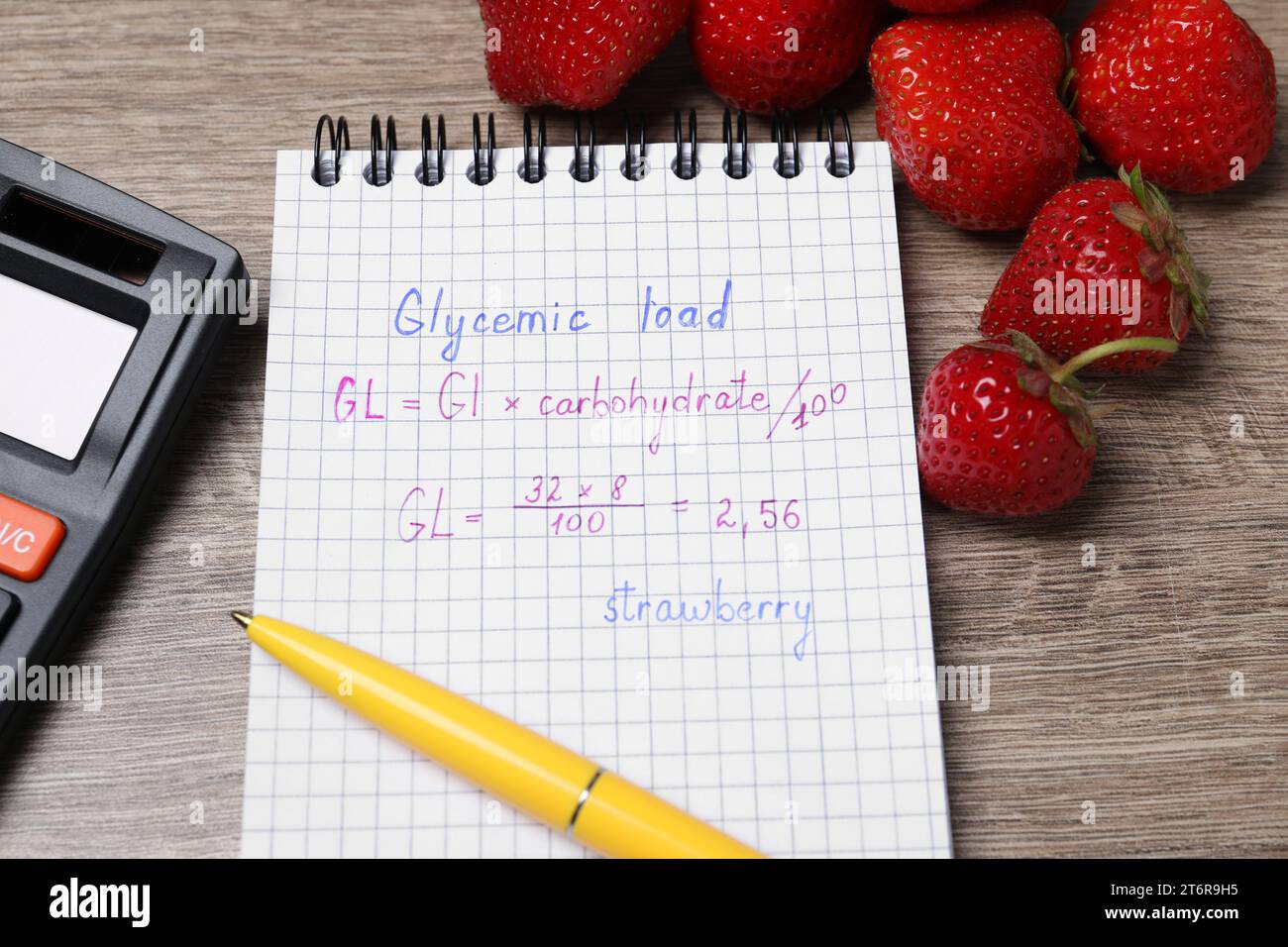 Notebook with calculated glycemic load for strawberry, pen and fresh berries on wooden table, closeup Stock Photo