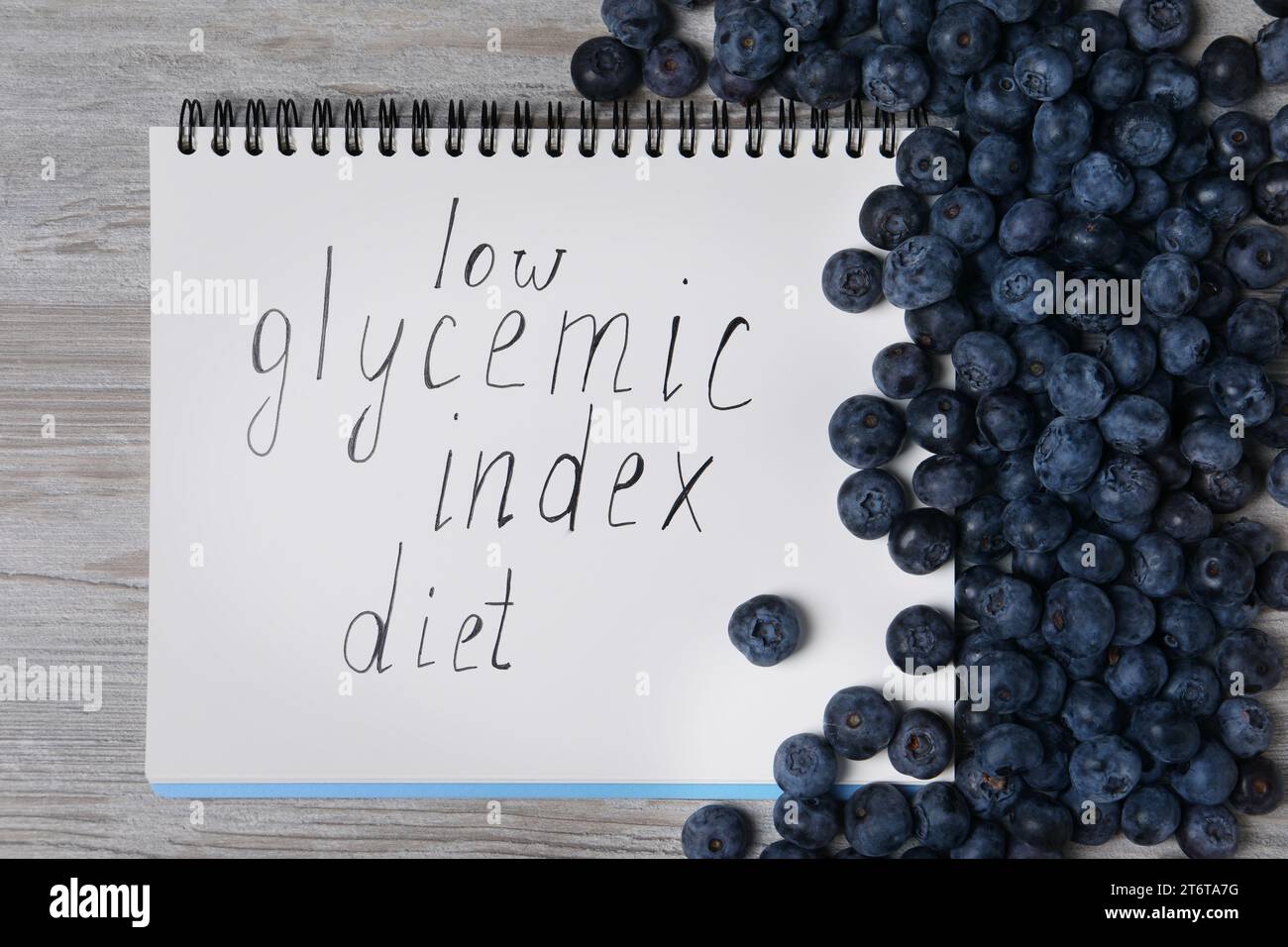 Notebook with words Low Glycemic Index Diet and blueberries on light wooden table, top view Stock Photo