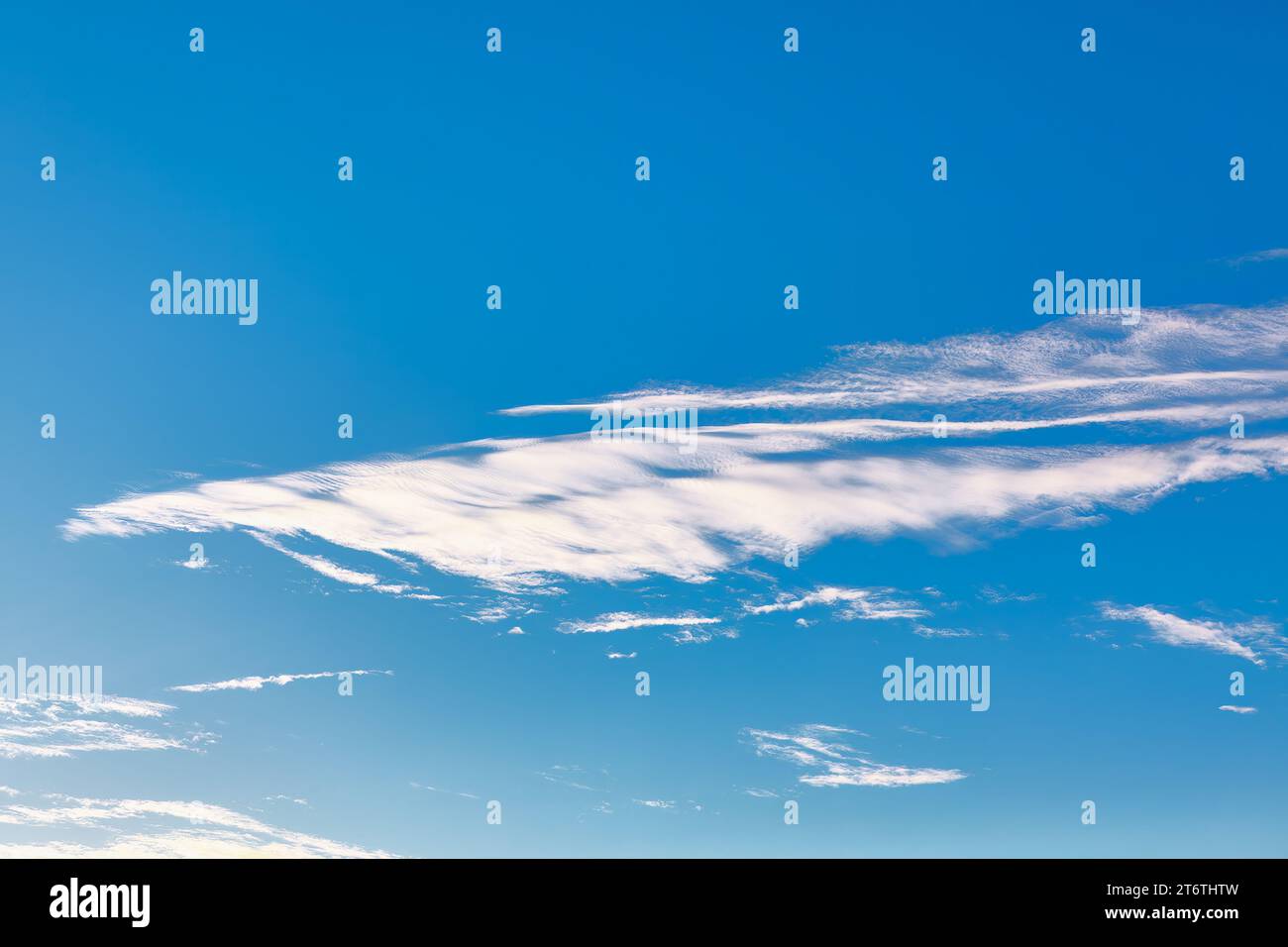Blue sky adorned with gentle, wispy white clouds . Blue hue is deep and calming, creating a sense of openness and tranquility Stock Photo