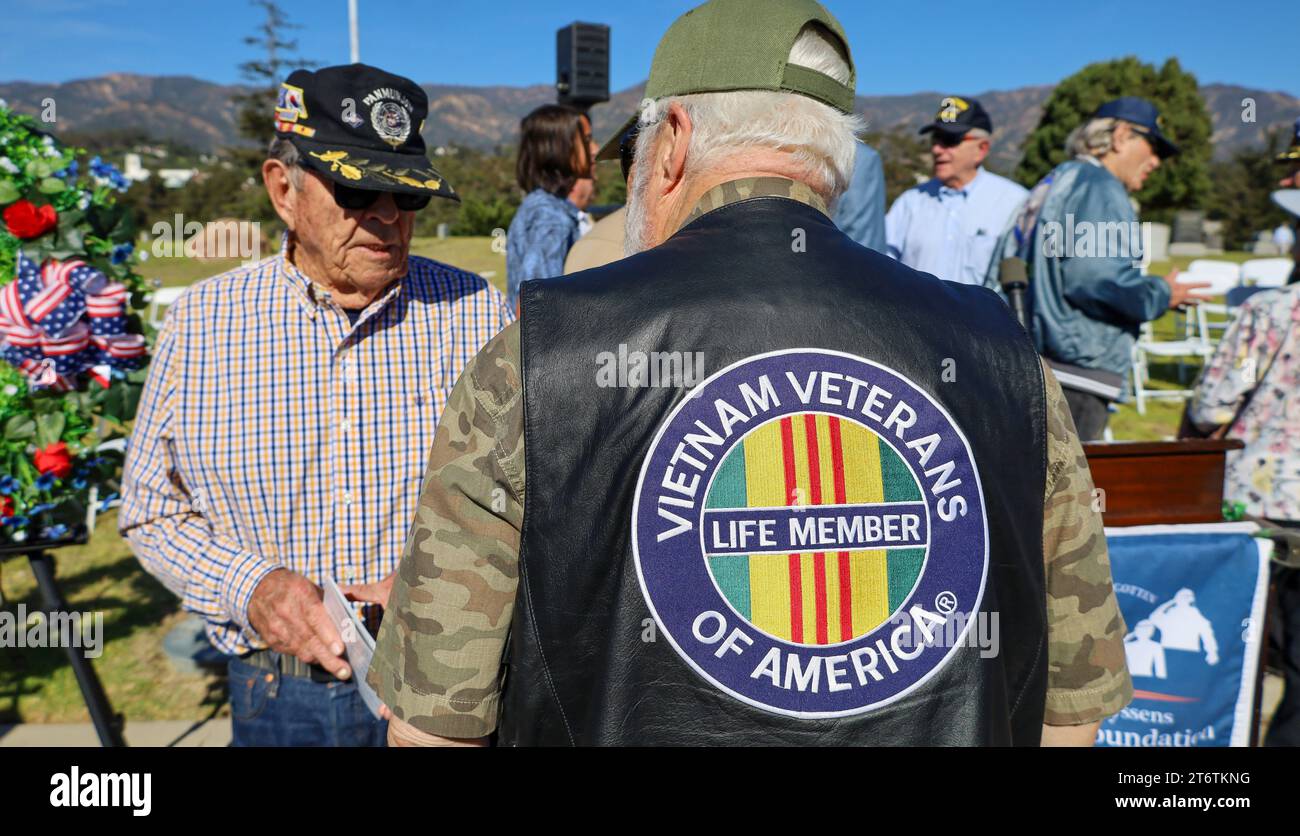 November 11, 2023, Santa Barbara, California, U.S: A Vet in a Vietnam Veterans of America Life Member vest and army shirt talks to another vet, at the end of the annual Veteranâ€™s Day Ceremony at Santa Barbara Cemetery, â€œHonoring all who have servedâ€, hosted by Pierre Claeyssenâ€™s Veterans Foundation. A beautiful green wreath with red roses is in the background. (Credit Image: © Amy Katz/ZUMA Press Wire) EDITORIAL USAGE ONLY! Not for Commercial USAGE! Stock Photo
