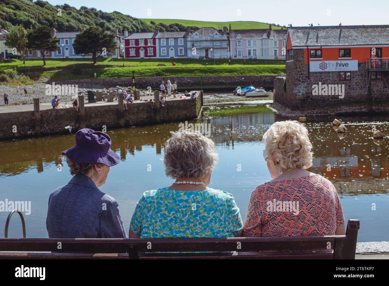 Three old ladies chat with each on a bench overlooking the water in Aberaeron in Wales Stock Photo