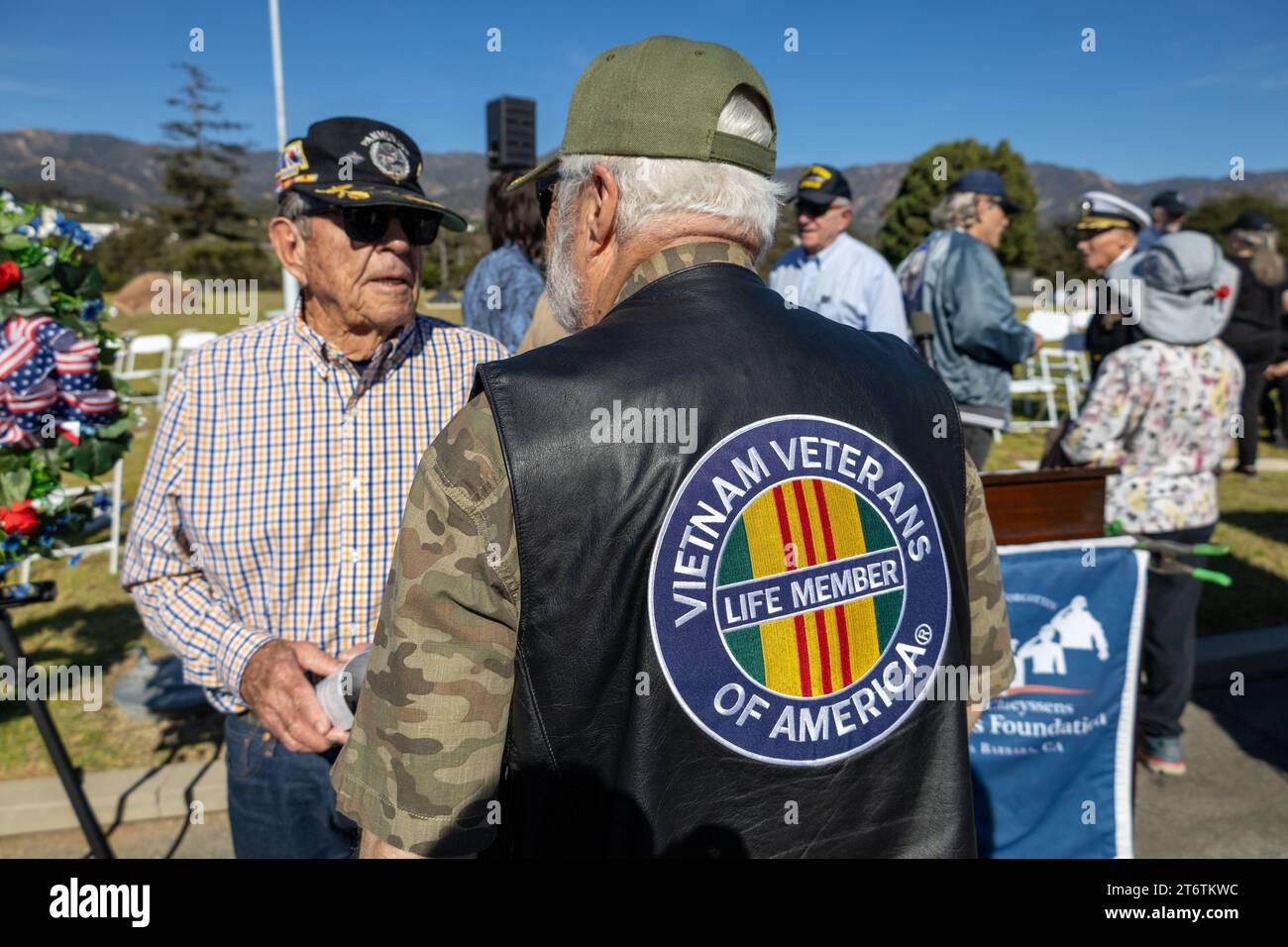 November 11, 2023, Santa Barbara, California, U.S: A Vet in a Vietnam Veterans of America Life Member vest and army shirt talks to another vet, at the end of the annual Veteranâ€™s Day Ceremony at Santa Barbara Cemetery, â€œHonoring all who have servedâ€, hosted by Pierre Claeyssenâ€™s Veterans Foundation. A beautiful green wreath with red roses is in the background. (Credit Image: © Amy Katz/ZUMA Press Wire) EDITORIAL USAGE ONLY! Not for Commercial USAGE! Stock Photo