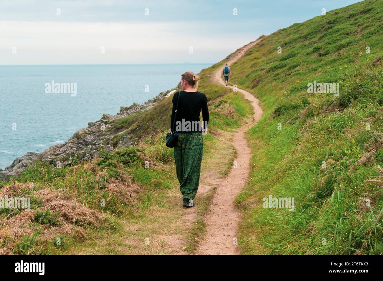 A woman in green trousers enjoys a walk on the coastal path near St Davids in Pembrokeshire in South Wales UK Stock Photo