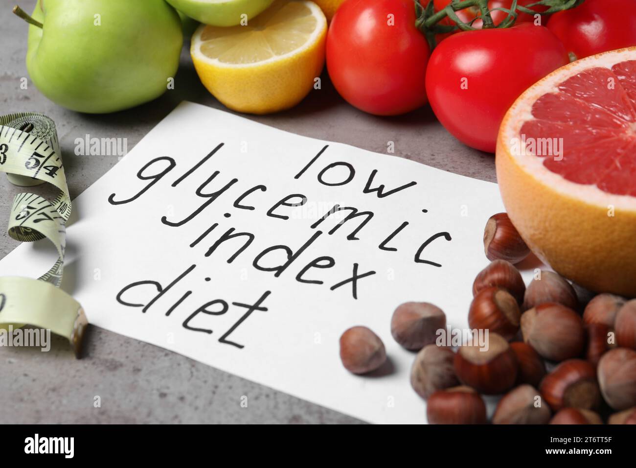 Paper with words Low Glycemic Index Diet, measuring tape and food on grey table, closeup Stock Photo