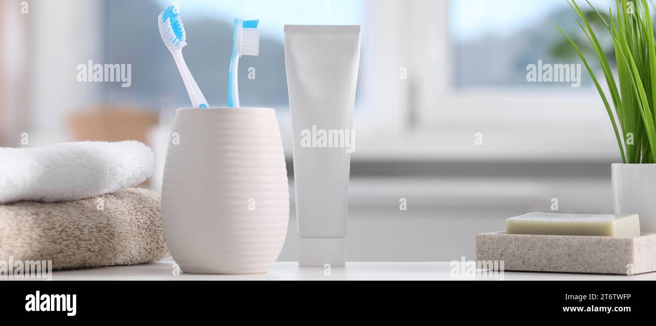 Plastic toothbrushes in holder, toothpaste, soap and towels on white table indoors, banner design Stock Photo