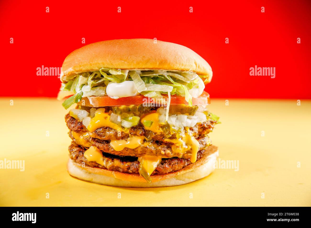 A closeup shot of a freshly-assembled hamburger on a wooden table, surrounded by accompaniments such as lettuce, tomatoes, pickles, and other cond Stock Photo