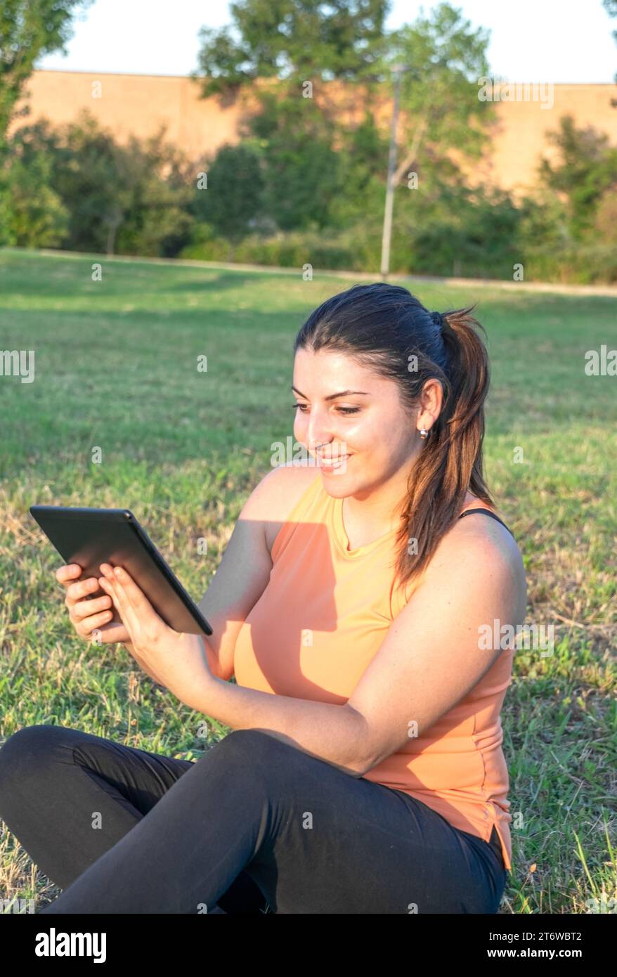 Young Caucasian woman smiling and happy using tablet sitting in park Stock Photo