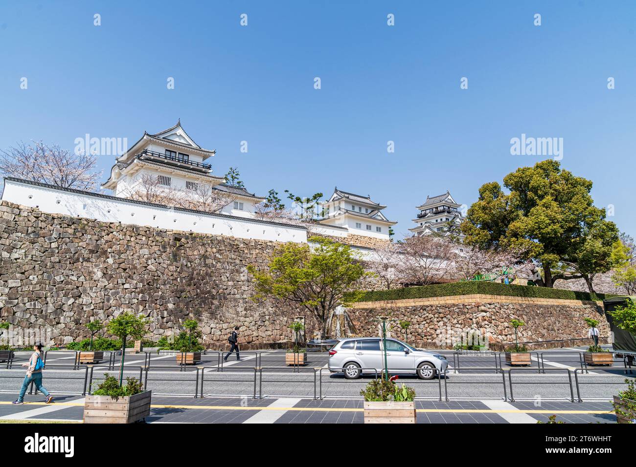 Fukuyama castle. Street view of the Ishigaki stone walls, white dobei plaster walls, two turrets and the castle keep with cherry blossoms and blue sky Stock Photo