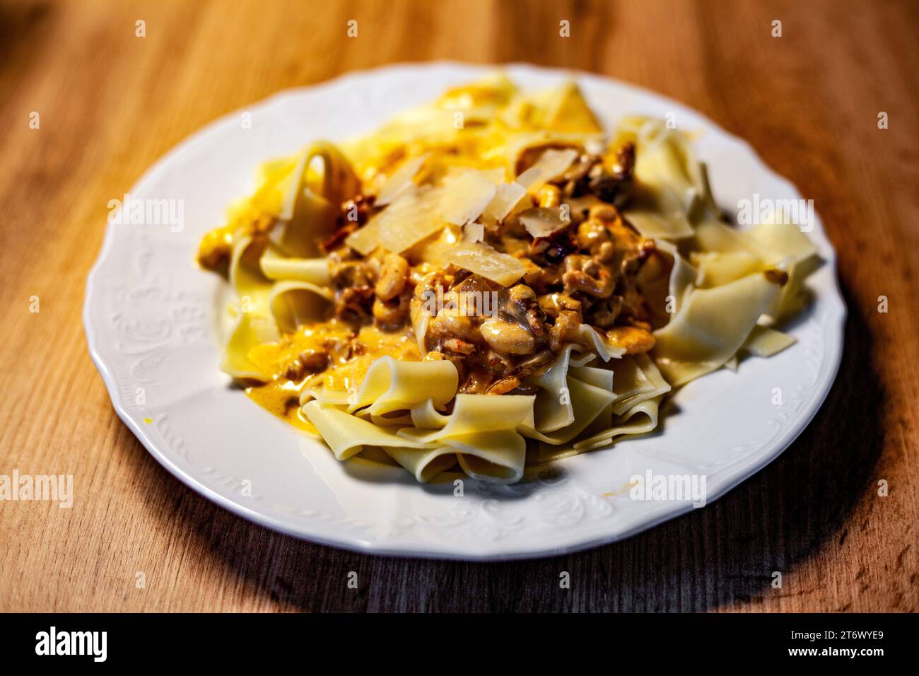 Italian food pasta with shrimp, cream, and parmesan in yellow color on white plate with blurred background on brown table with wood pattern and texture Stock Photo