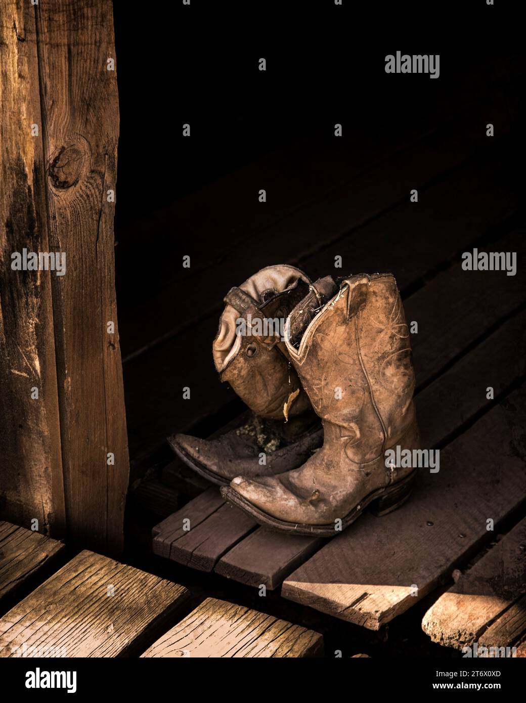 Old and worn leather cowboy boots rest in an open door. Stock Photo