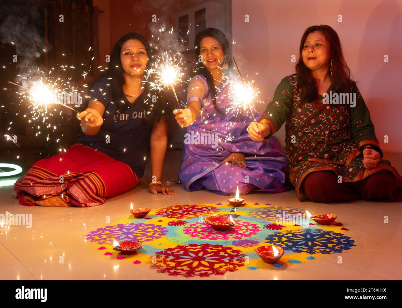 Women light phuljhari or stick firecrackers sitting next to a rongoli