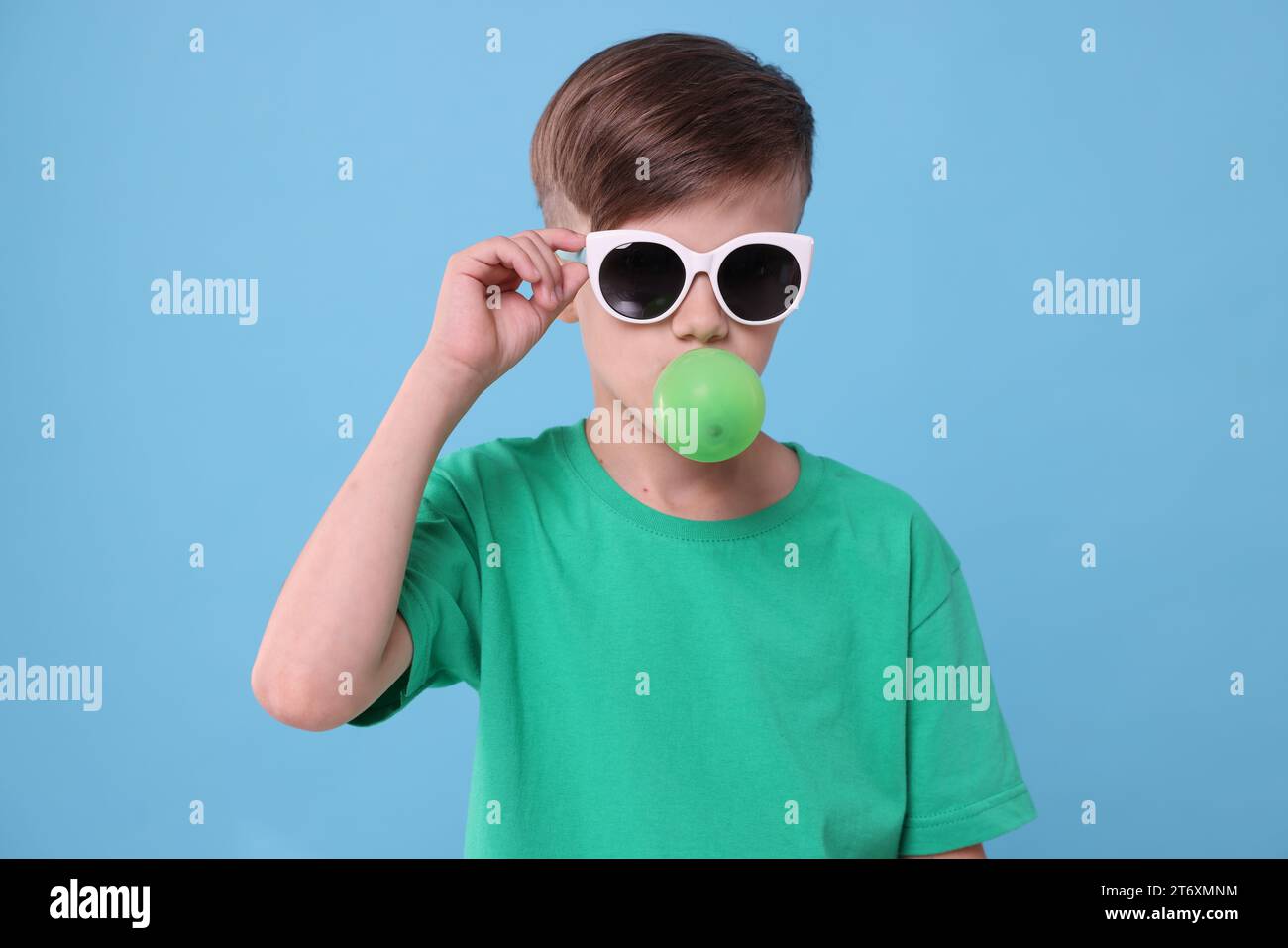 Boy in sunglasses blowing bubble gum on light blue background Stock ...