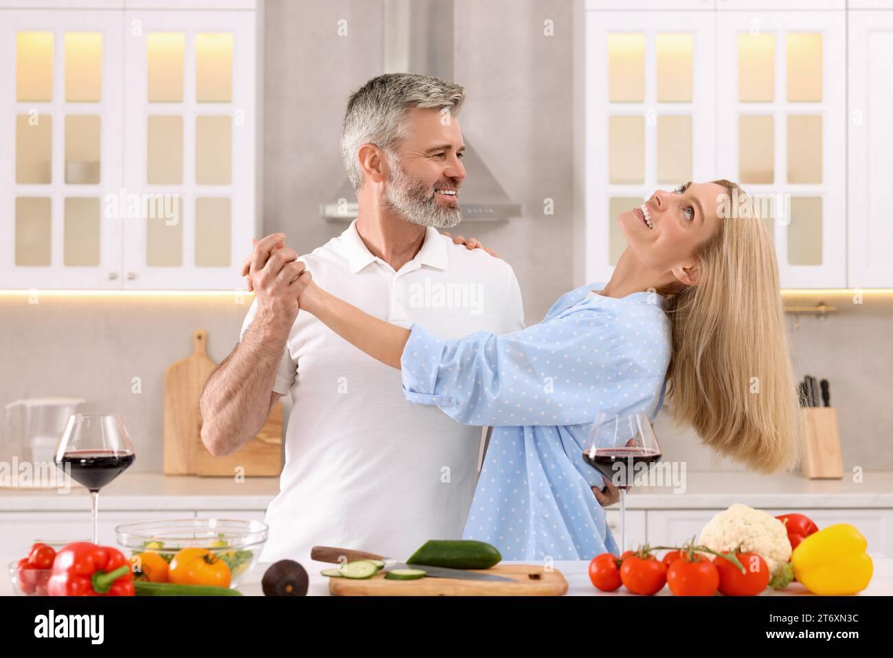 Happy affectionate couple dancing while cooking together in kitchen Stock Photo