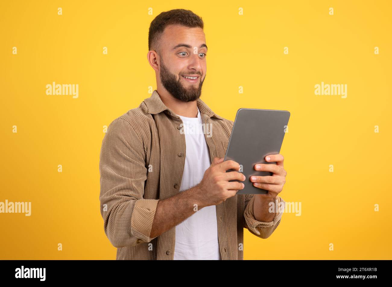 Shocked funny european millennial man with beard look at tablet, using app for social networks Stock Photo