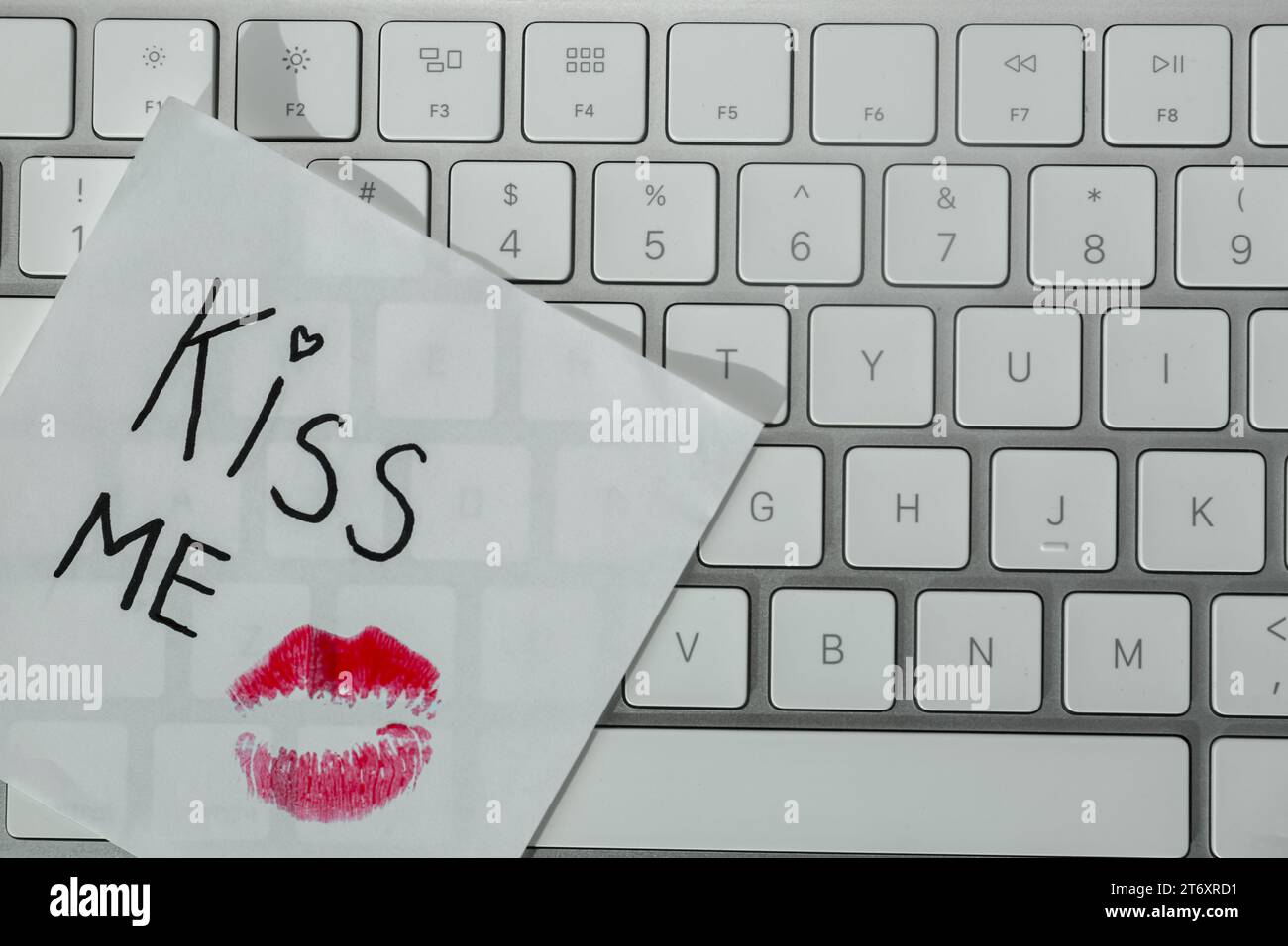 Sticky note with phrase Kiss Me and lipstick mark on keyboard, top view
