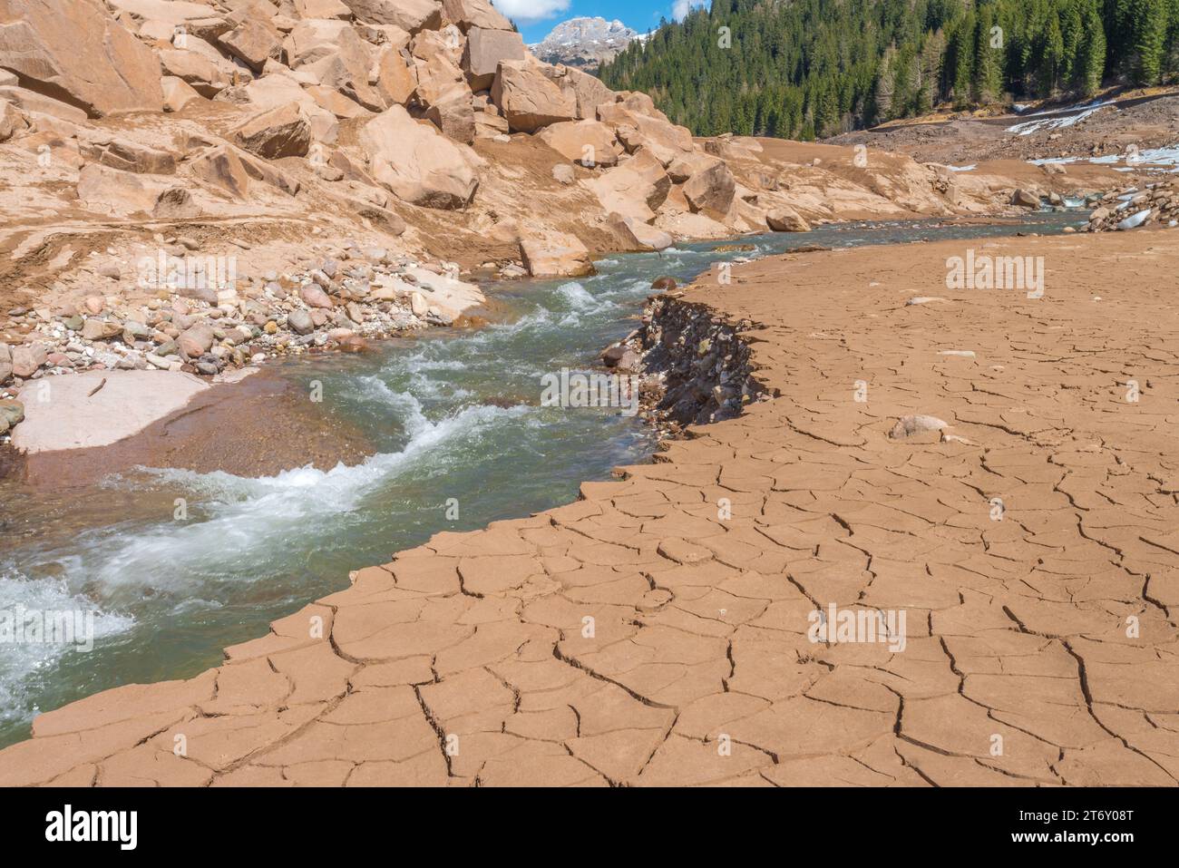 Drought effects visible along running mountain stream, with dry mud and