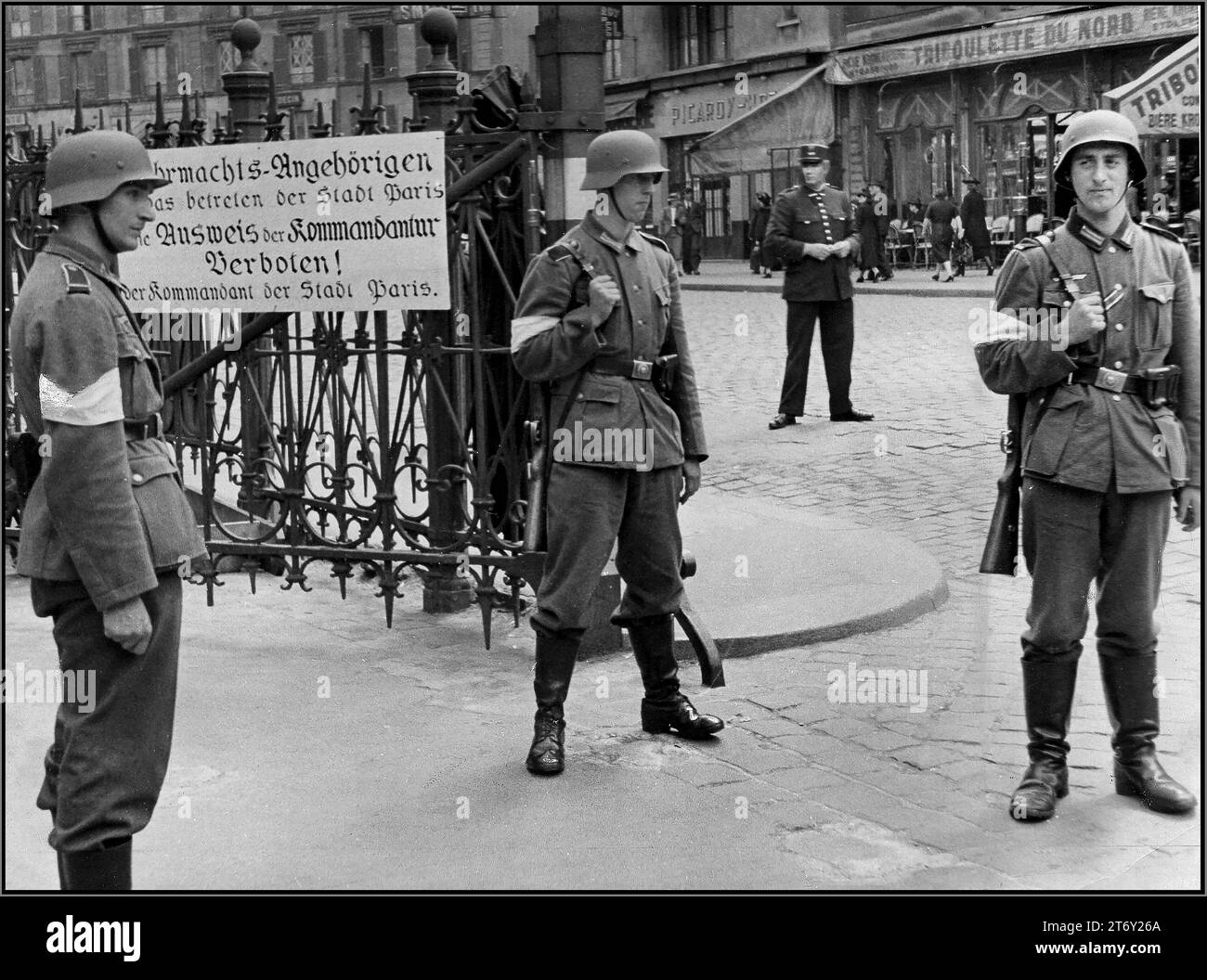 WW2 PARIS OCCUPATION by Nazi Germany. 1940s Wehrmacht soldiers stand guard at Nazi Commandant Office Paris with French Policeman behind. Sign reads Wehrmacht Members entering the city of Paris Identification from the commandants office. FORBIDDEN ! Occupied Paris France 1940s World War II WW2 Second World War Stock Photo