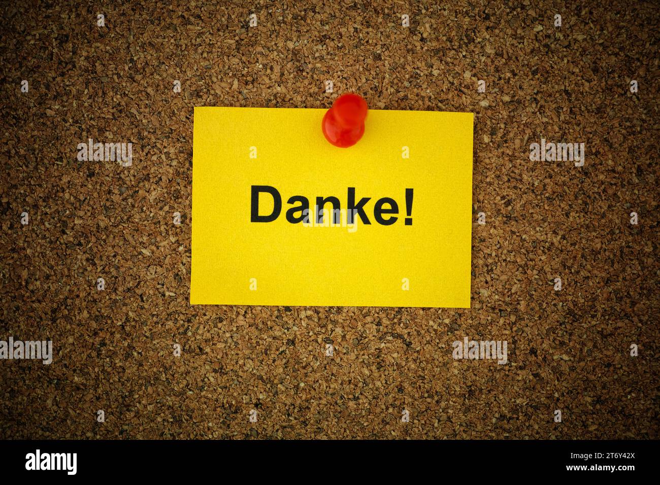 A yellow paper note with the word Danke! (Thank you in German) on it pinned to a cork board. Close up. Stock Photo