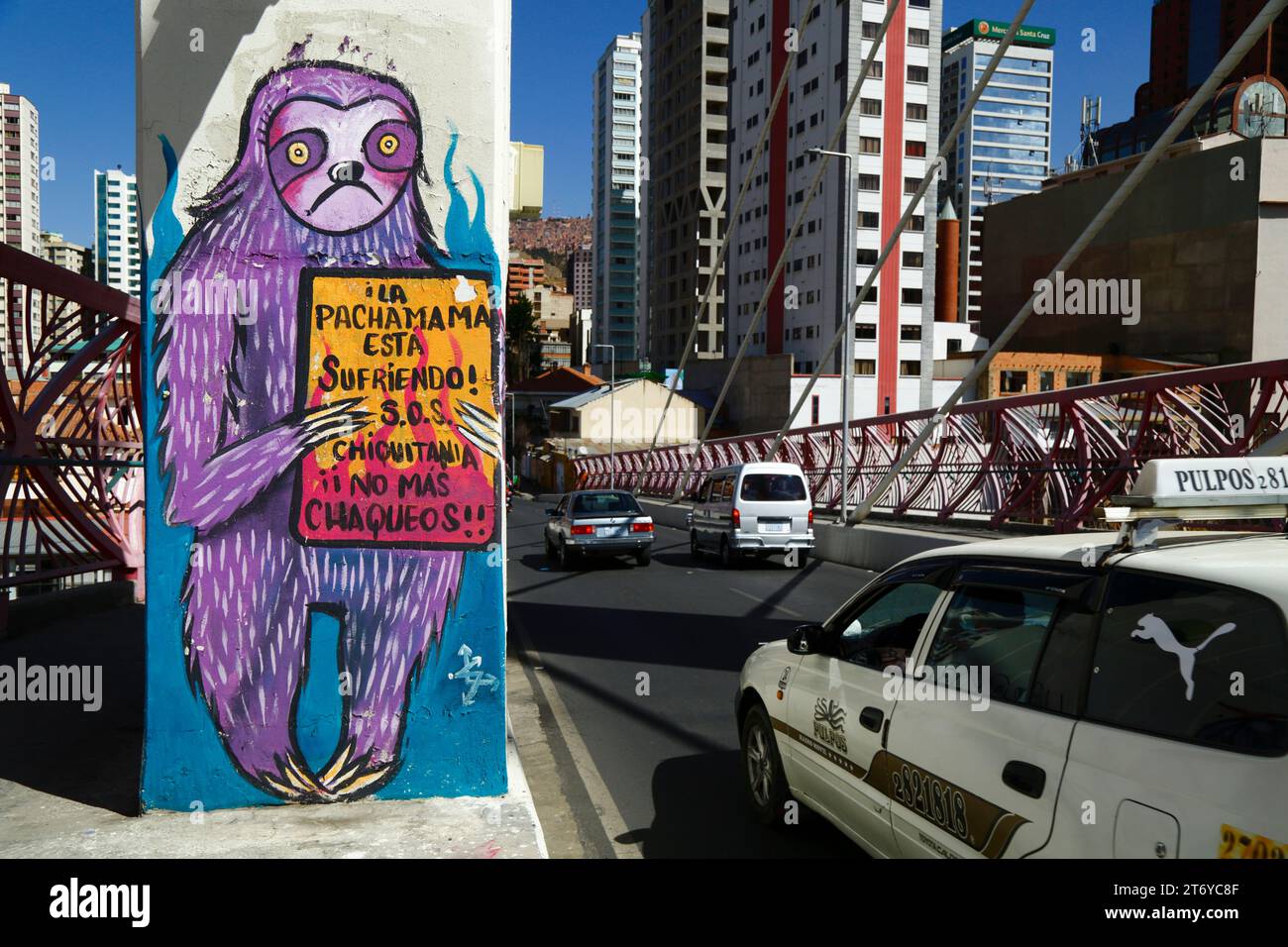 La Paz, Bolivia, 7th July 2022: A taxi drives past a mural on a pillar of the Puente Gemelo / Twin Bridge of a sloth protesting against chaqueos / fires started deliberately to clear the tropical forests of he Chiquitania and Amazon regions of the Bolivian lowlands. Deforestation has become a huge problem in Bolivia in the last decade in particular; in 2022, Global Forest Watch placed Bolivia third in the world for primary forest loss. Much of the deforestation is government policy to expand the country's agricultural frontier to produce soya and cattle for export to especially China. Stock Photo