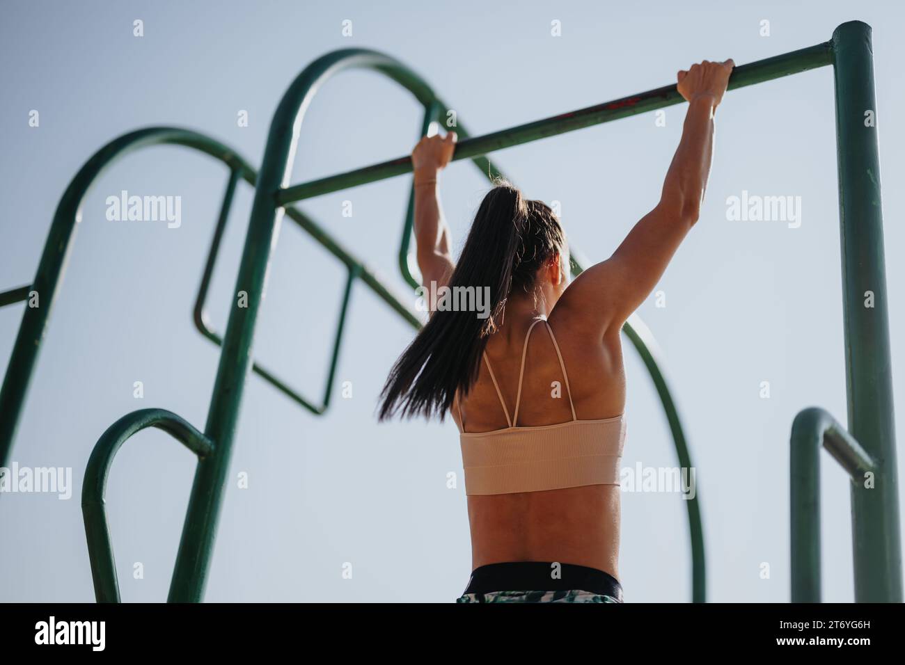 Caucasian girl doing pull ups on metal bars in a park. She exercise ...