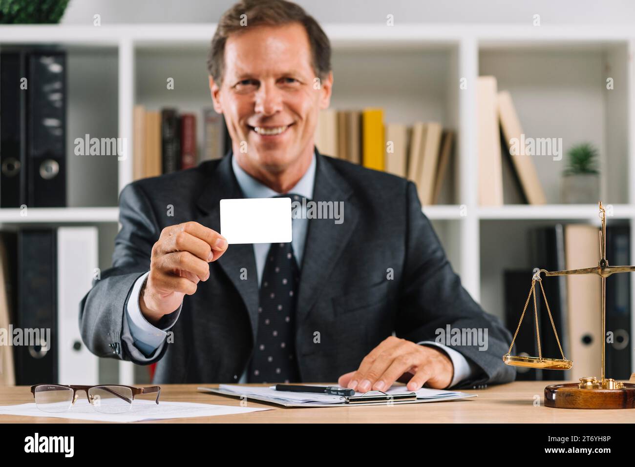 Smiling mature lawyer showing blank visiting card sitting court room Stock Photo
