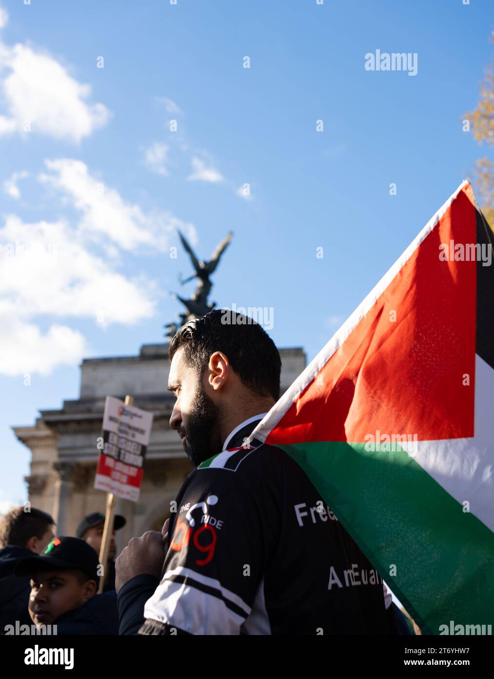 Man holds Palestinian flag in front of London's Wellington Arch during the peace march. The autumn sun catches his face and hair with a hard light. Stock Photo