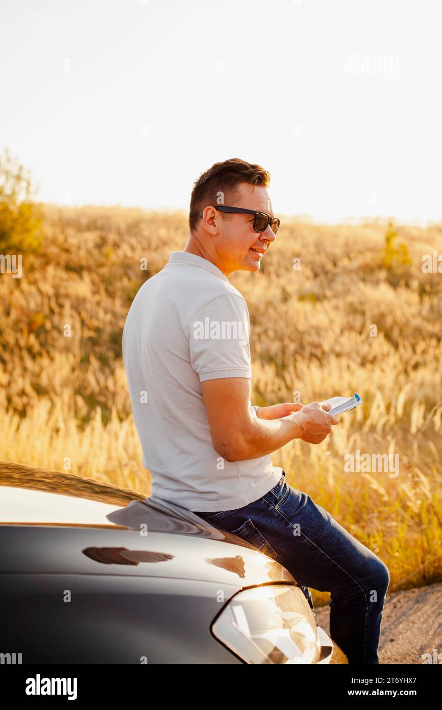 Young man reading book car hood Stock Photo