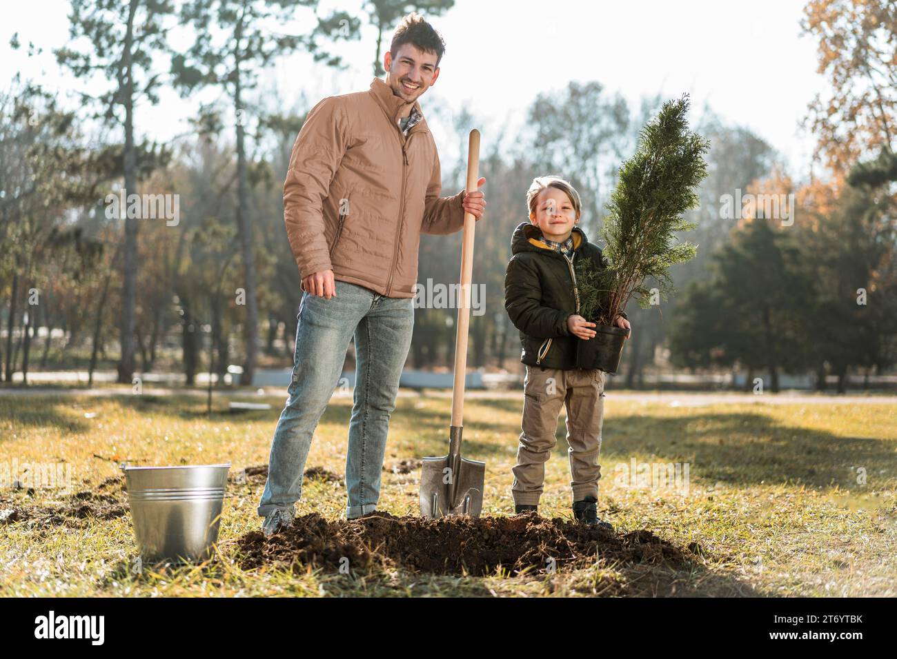 Man using shovel dig hole planting tree while posing son Stock Photo