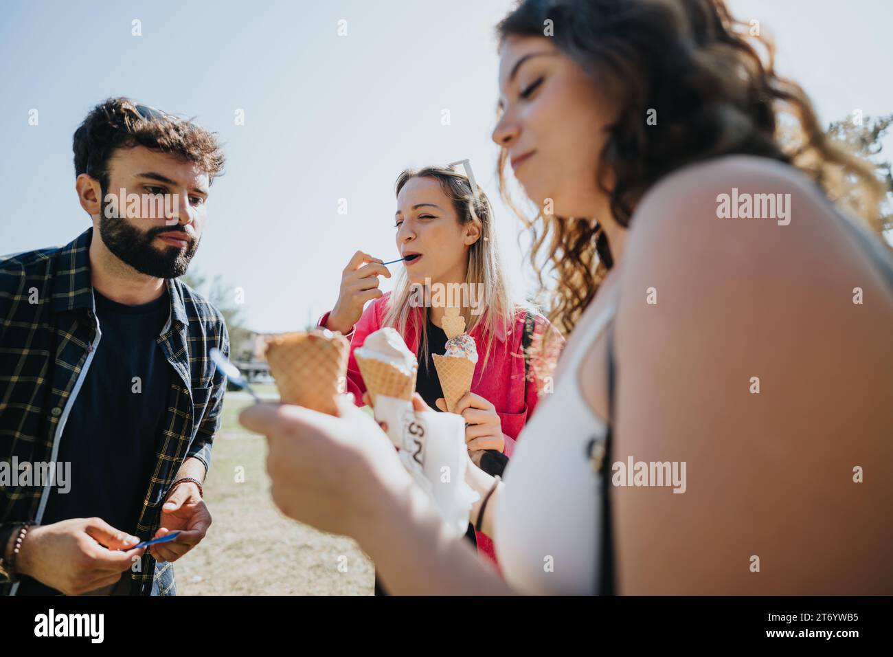 Carefree friends enjoying a sunny day in a green park, eating ice cream ...