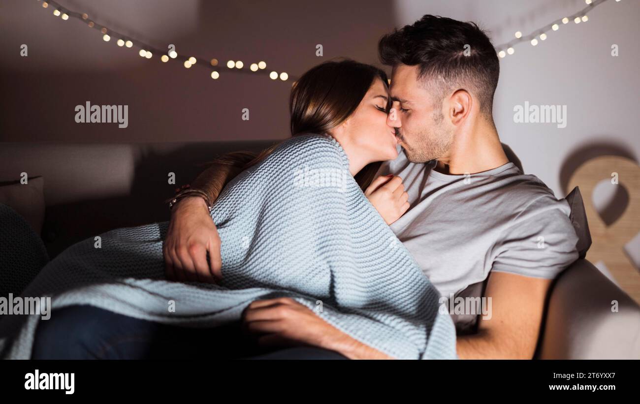 Young man kissing with woman lying sofa Stock Photo