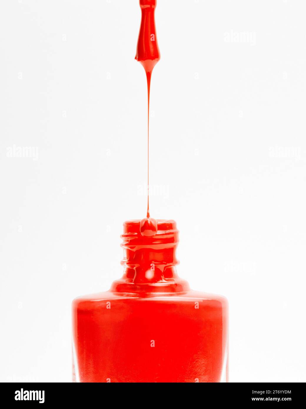 Beautiful red colored nail polish dripping from brush into bottle white backdrop Stock Photo