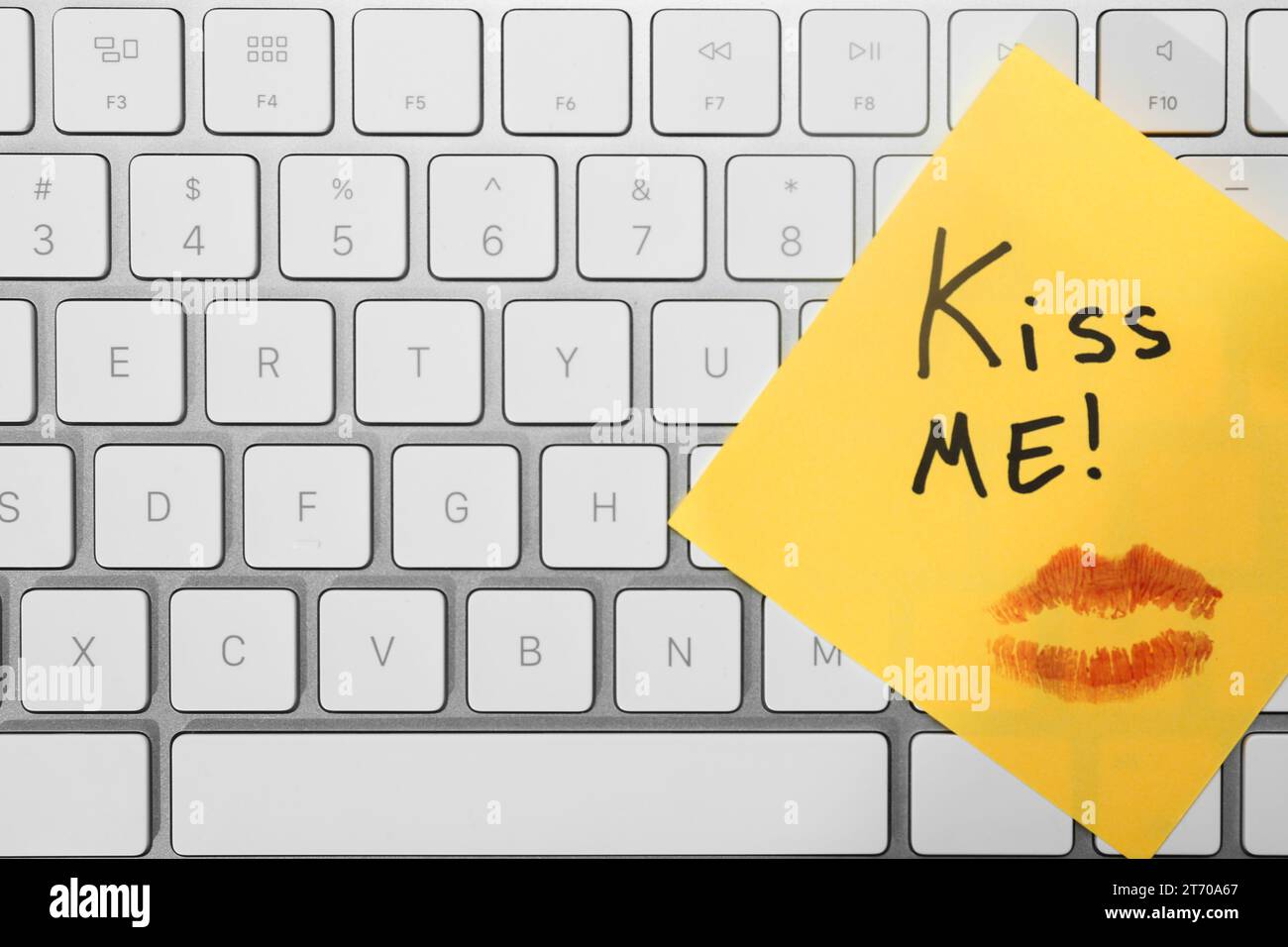 Sticky note with phrase Kiss Me and lipstick mark on keyboard, top view