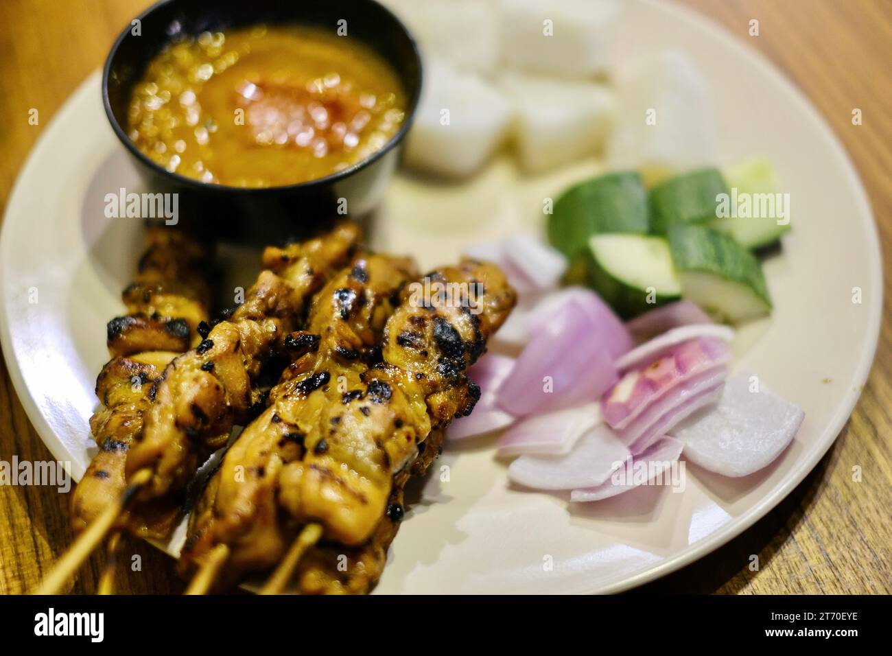Chicken satay skewers with red onion, cucumber slices and rice cakes