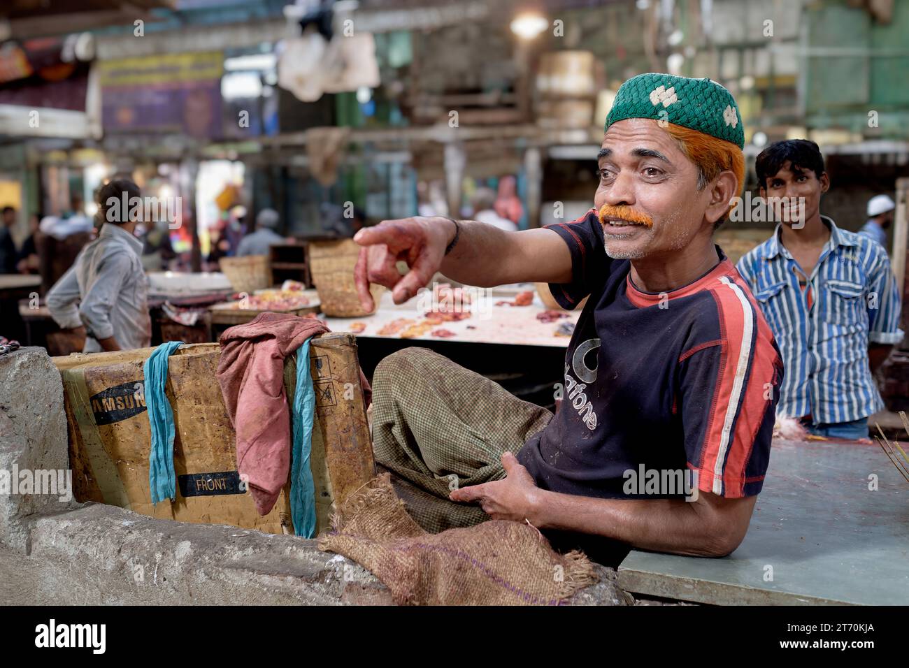 A Muslim butcher in a halal slaughterhouse in Mumbai, India, wearing a green Muslim cap and and henna-colored hair gesticulating towards a colleague Stock Photo