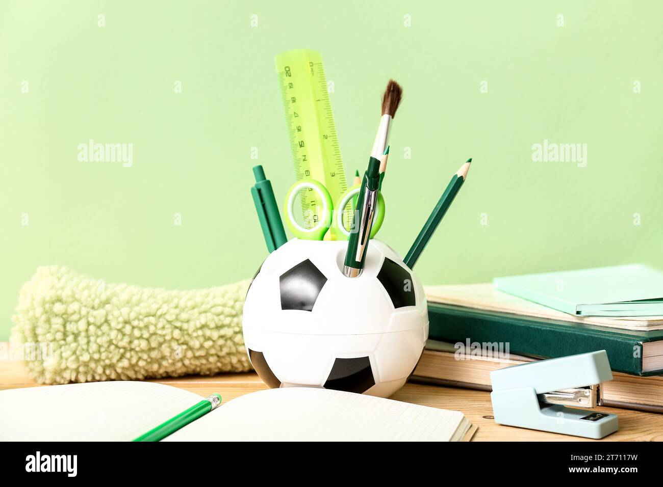 Holder in shape of soccer ball with different stationery and notebooks on wooden desk, closeup Stock Photo