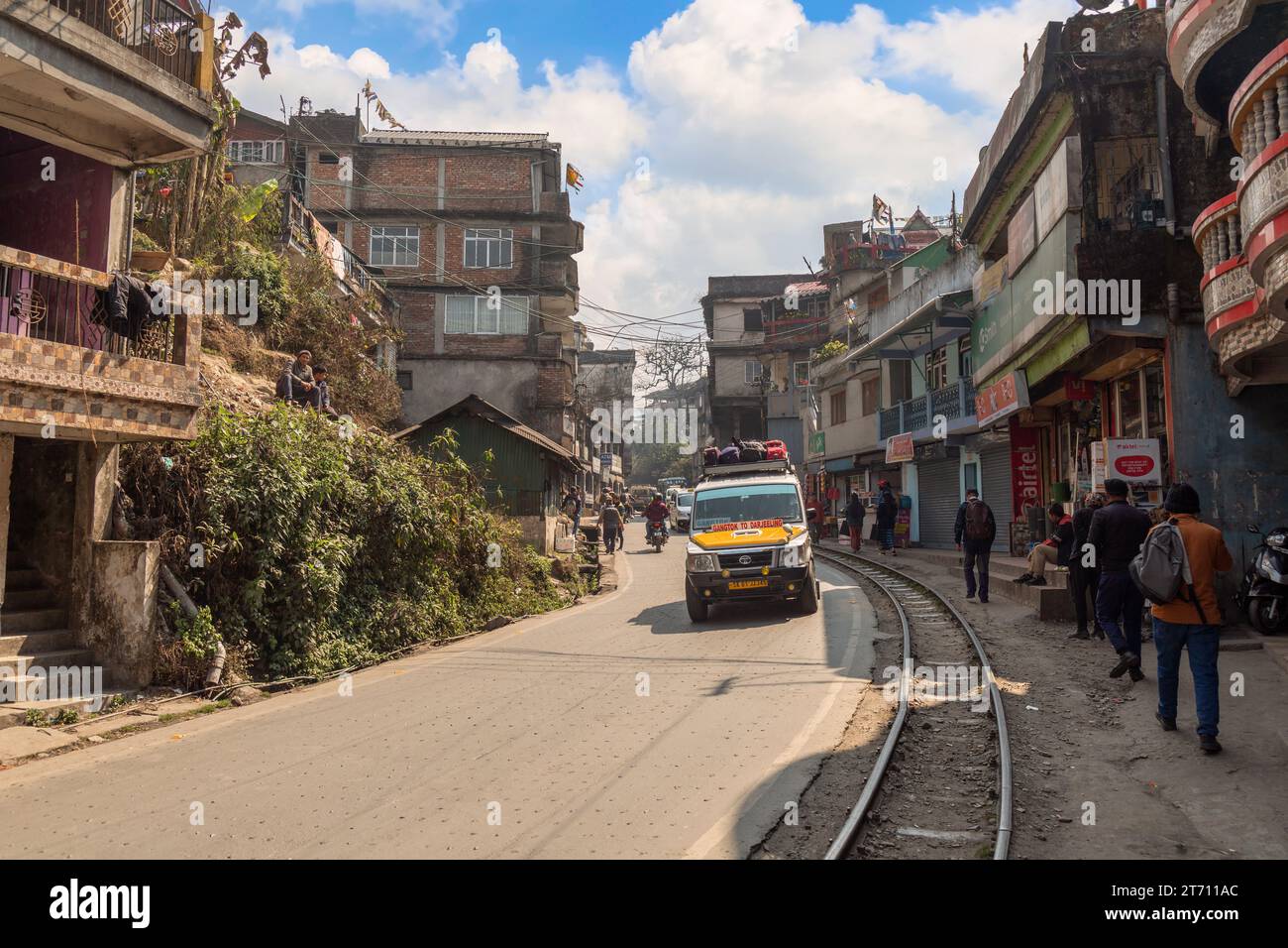 Darjeeling city road with toy train tracks, shops, and tourists. Darjeeling is popular hill station in the state of West Bengal, India. Stock Photo