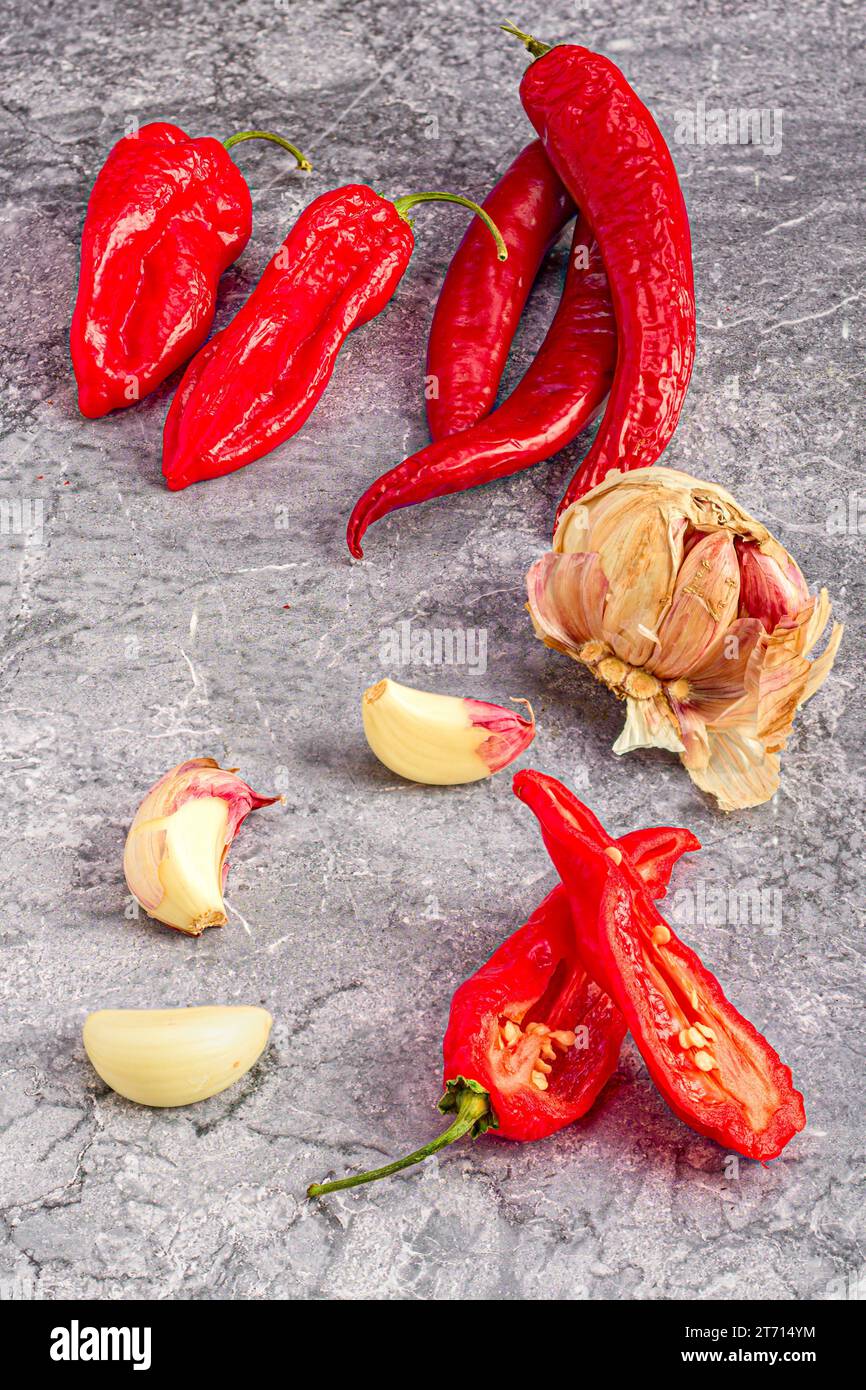A close-up shot of a pile of freshly-picked red peppers and garlic cloves on a grey cement surface Stock Photo