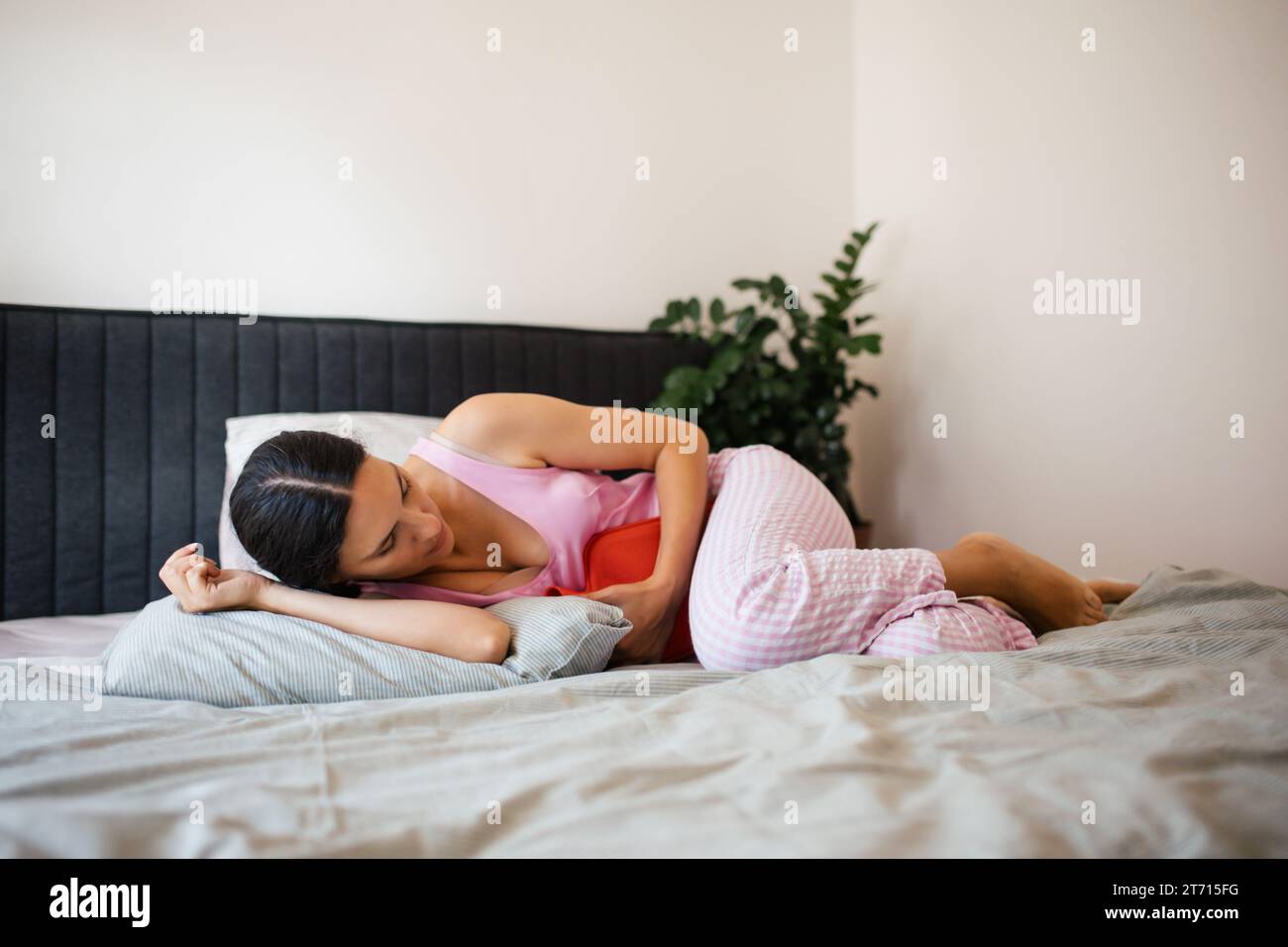 Woman at home suffering from menstrual pain. Menstrual cramps, woman warming lower abdomen with