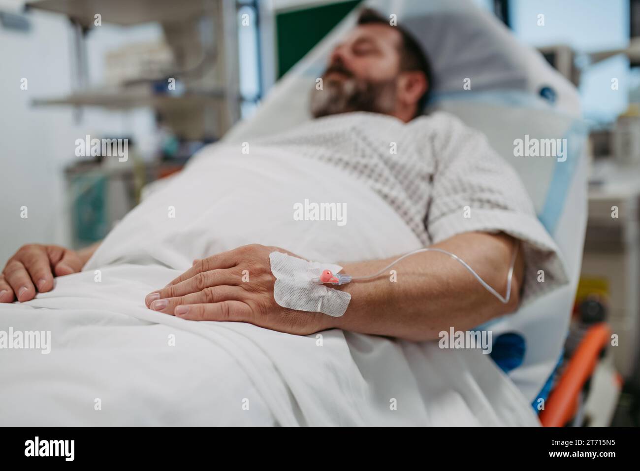 Patient with IV cannula in vein, hand lying in hospital bed. Man in