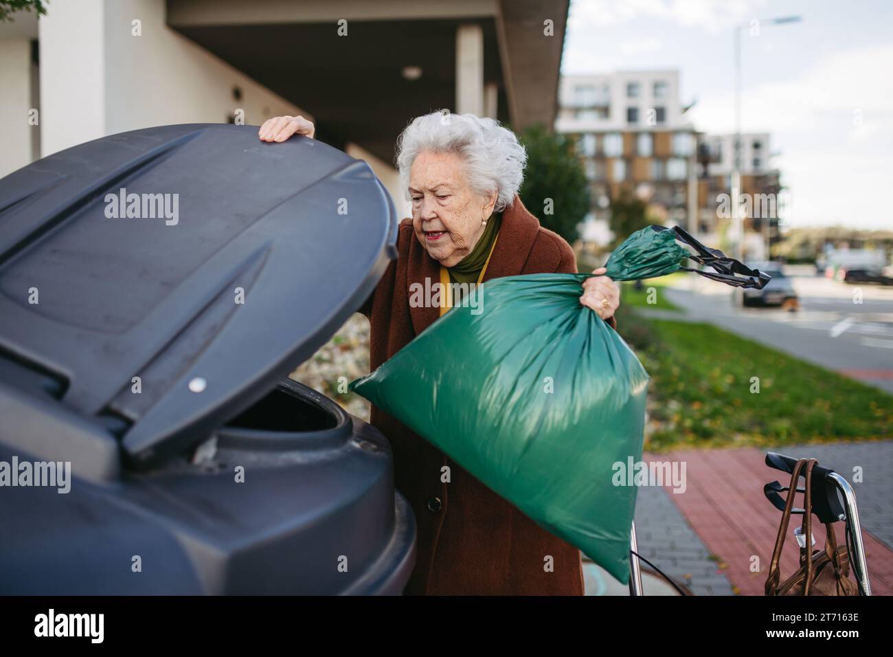 Elderly woman disposing of trash into the garbage can, waste container