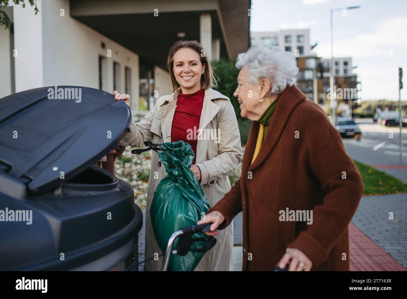 Woman helping elderly neighbor throw away trash into garbage can, waste