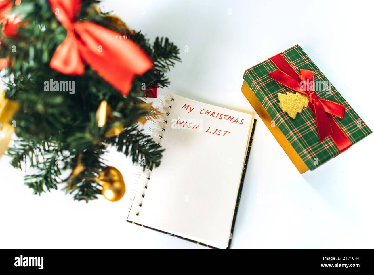 open notepad with christmas wish list text. decorated christmas tree and gift box on background. Stock Photo