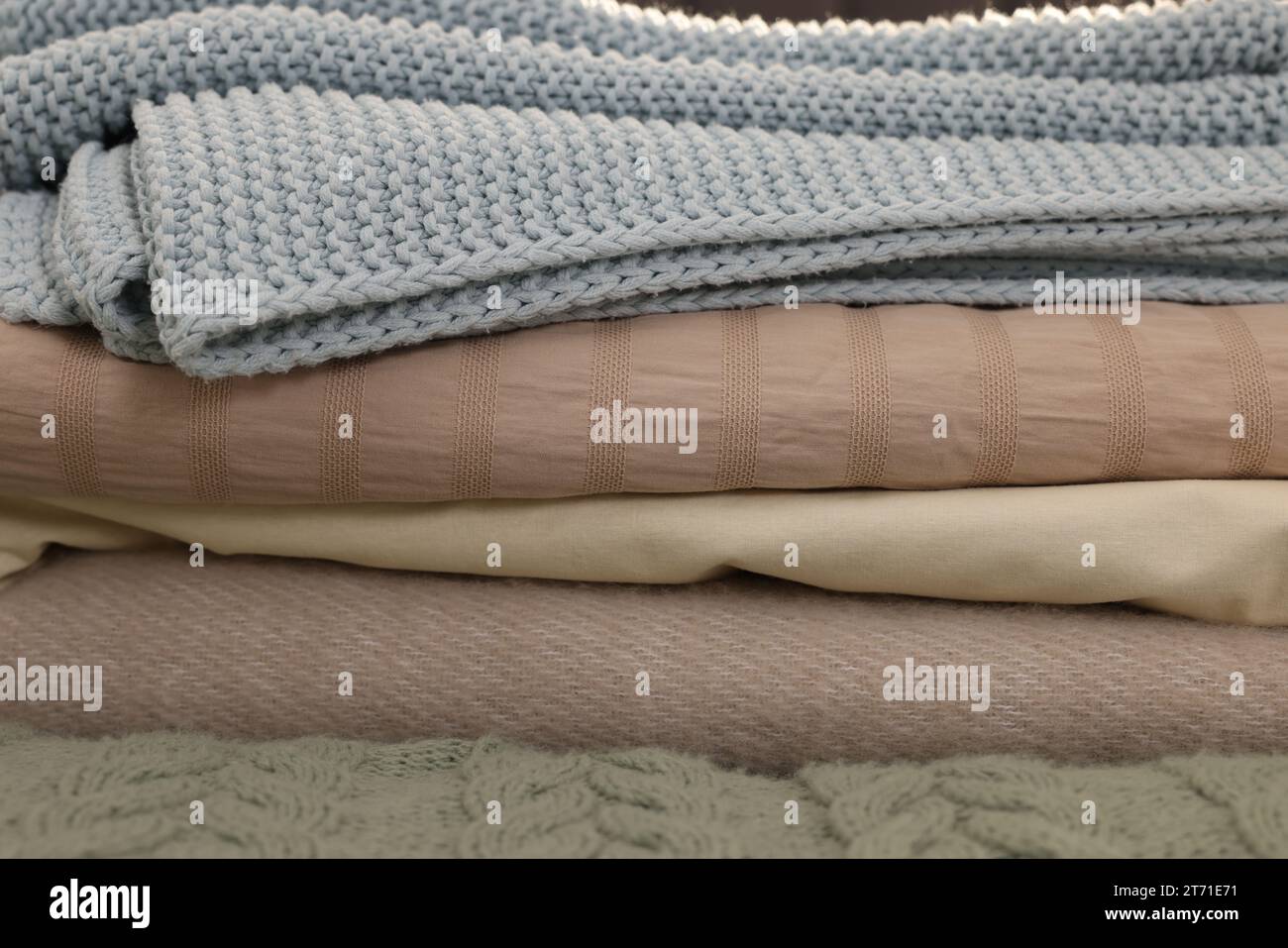 Stack of different folded blankets on bed, closeup. Home textile Stock Photo
