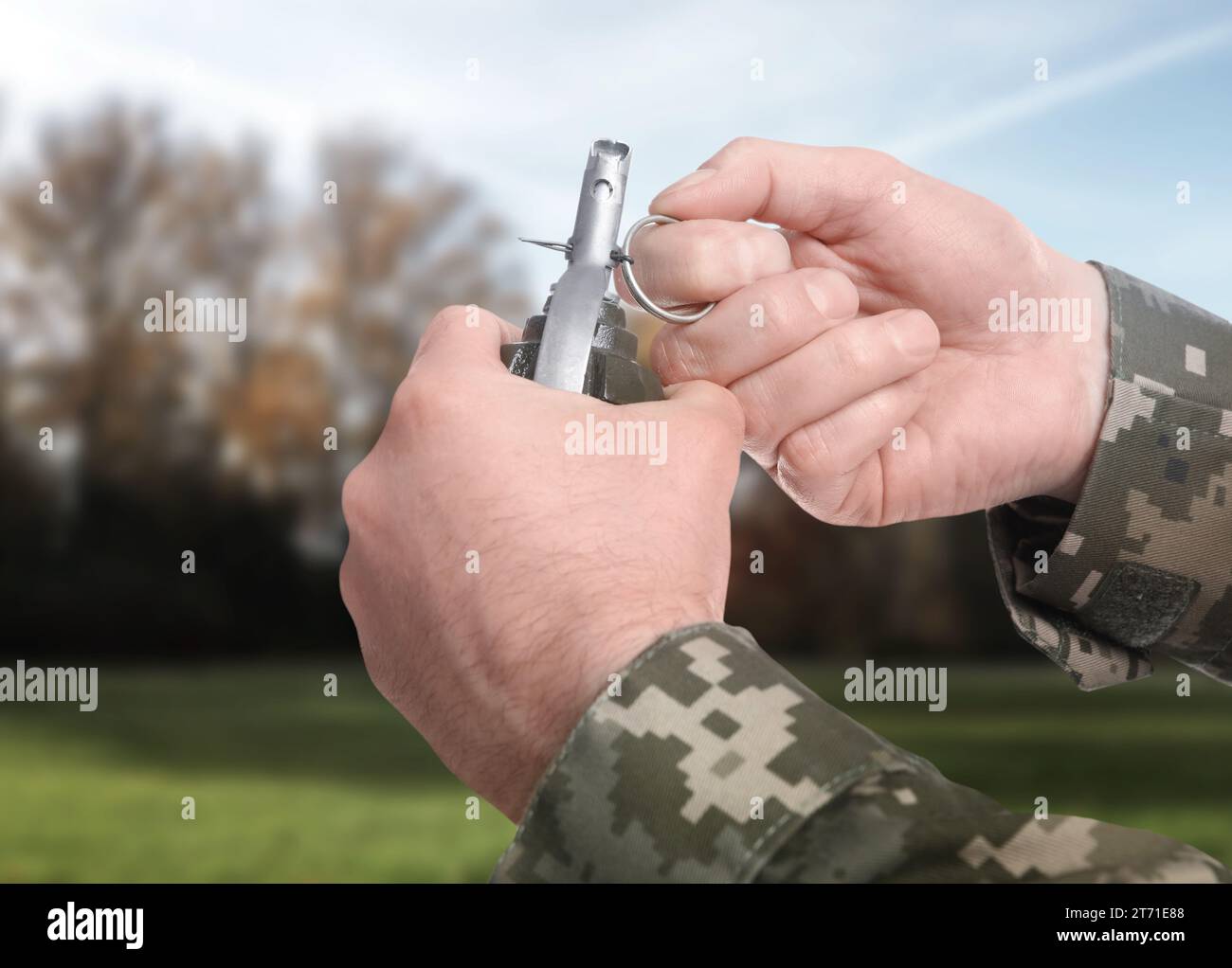 Soldier pulling safety pin out of hand grenade outdoors, closeup Stock