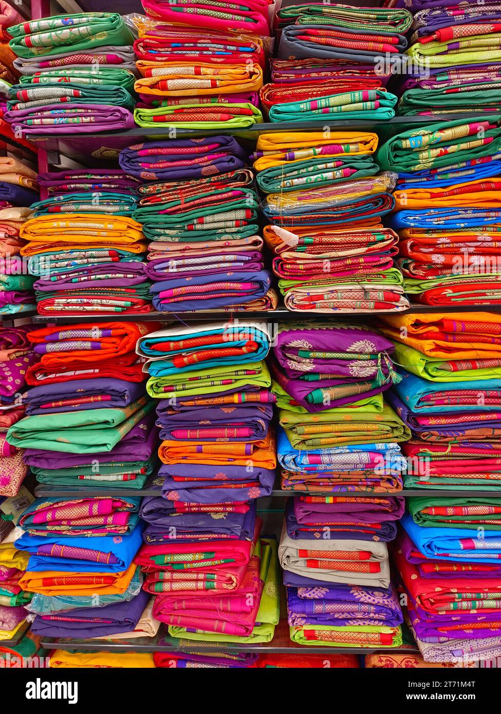 Neatly stacked colorful silk saris in racks in a textile shop, These exquisite, expensive sarees are famous for their gold and silver zari, brocade. I Stock Photo
