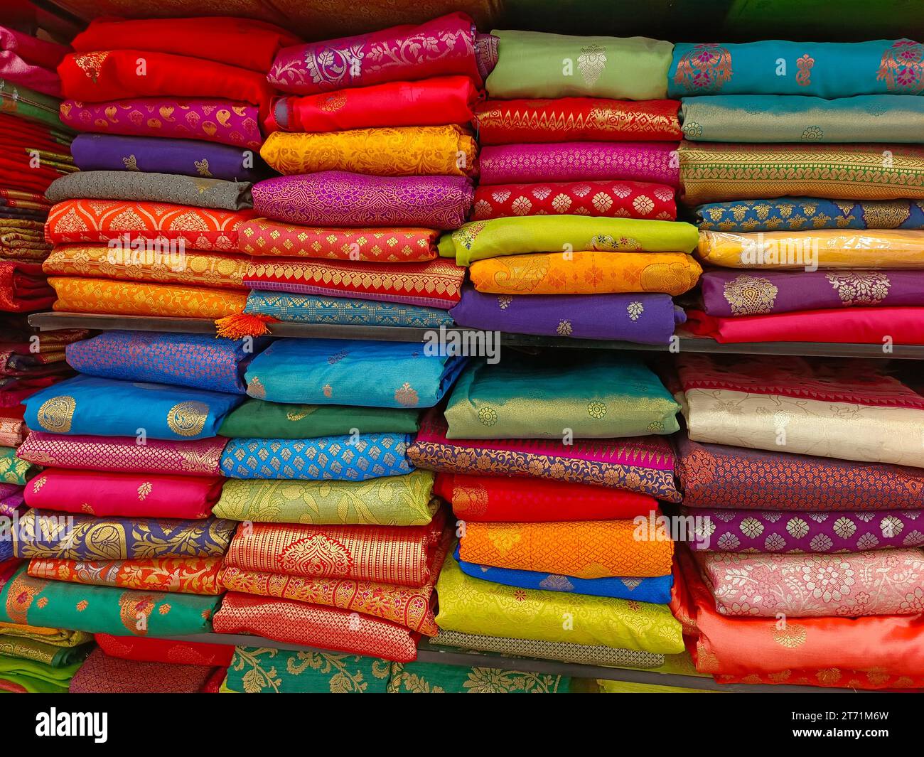 Neatly stacked colorful silk saris in racks in a textile shop, These exquisite, expensive sarees are famous for their gold and silver zari, brocade. I Stock Photo