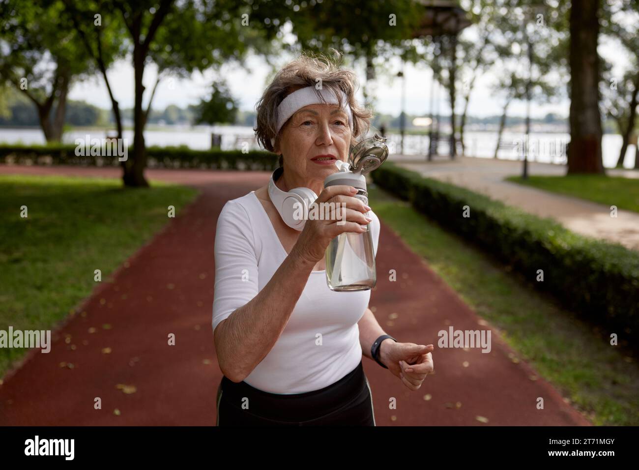 Elderly woman drinking water taking short break during running exercise Stock Photo