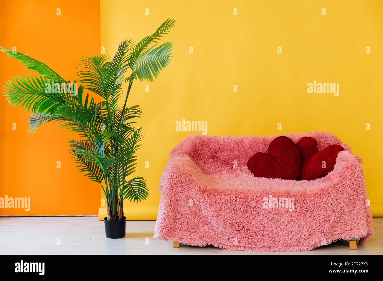 pink sofa with red pillows and decorative flower on a yellow background Stock Photo